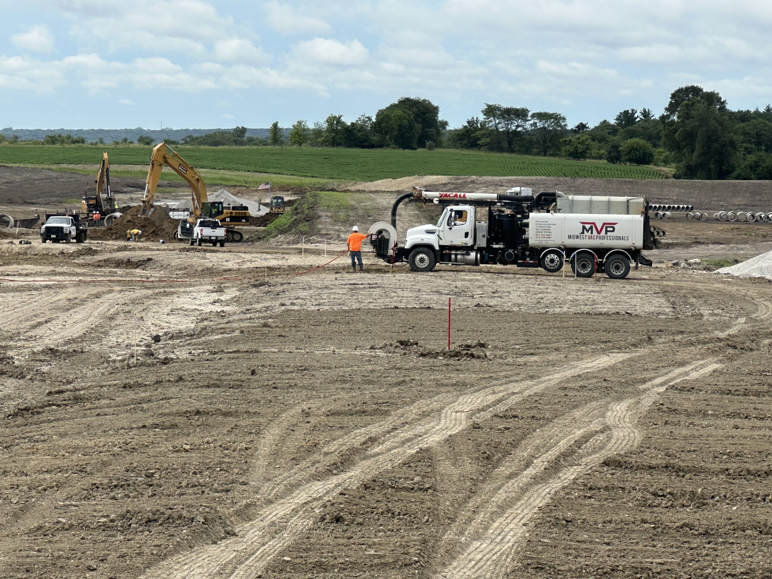 MVP vacuum truck with excavators working an open dirt site during land development, with farmland in the background.