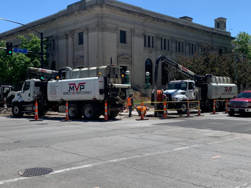 Two MVP vacuum trucks working together on a downtown street in front of a historic government building, with traffic cones marking the work zone.